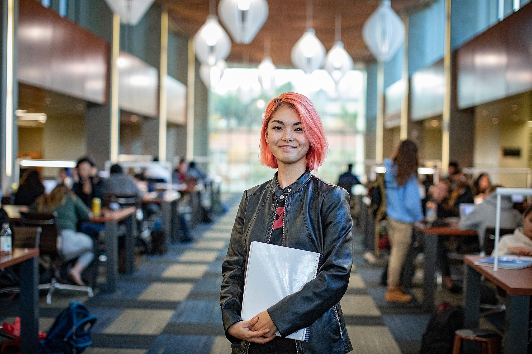 Female student with pink hair standing and posing in the library