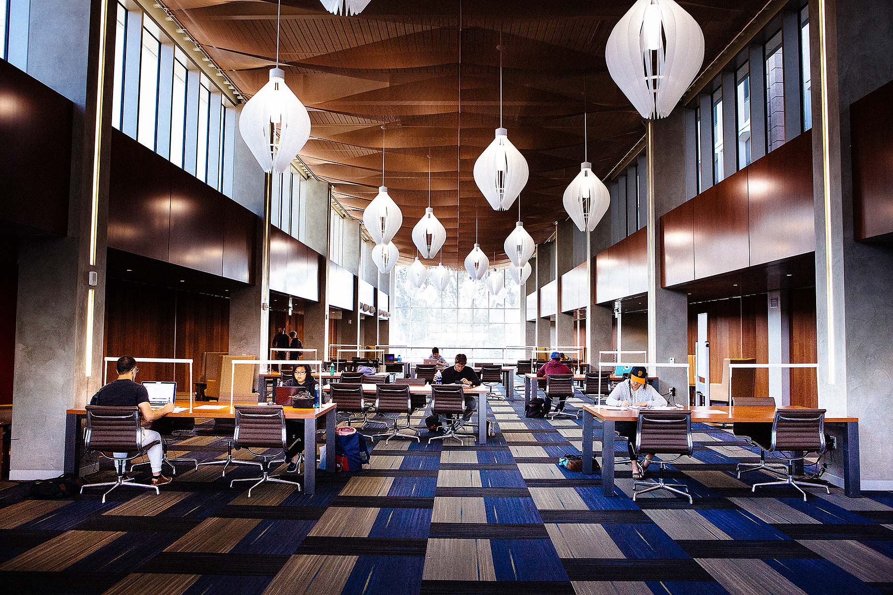 Panoramic view of UCSB library with students at desks and haning chandeliers